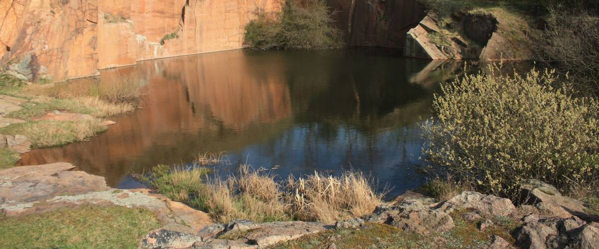 A natural landscape with a pond, rocky cliffs, and sparse vegetation.