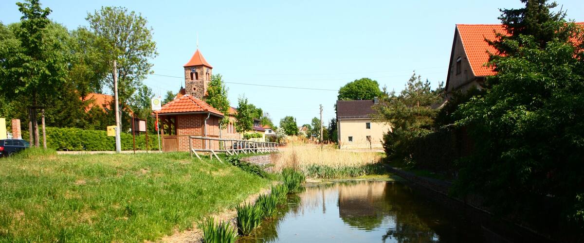 A calm river with a brick wall on one side and a church with a red roof in the background.
