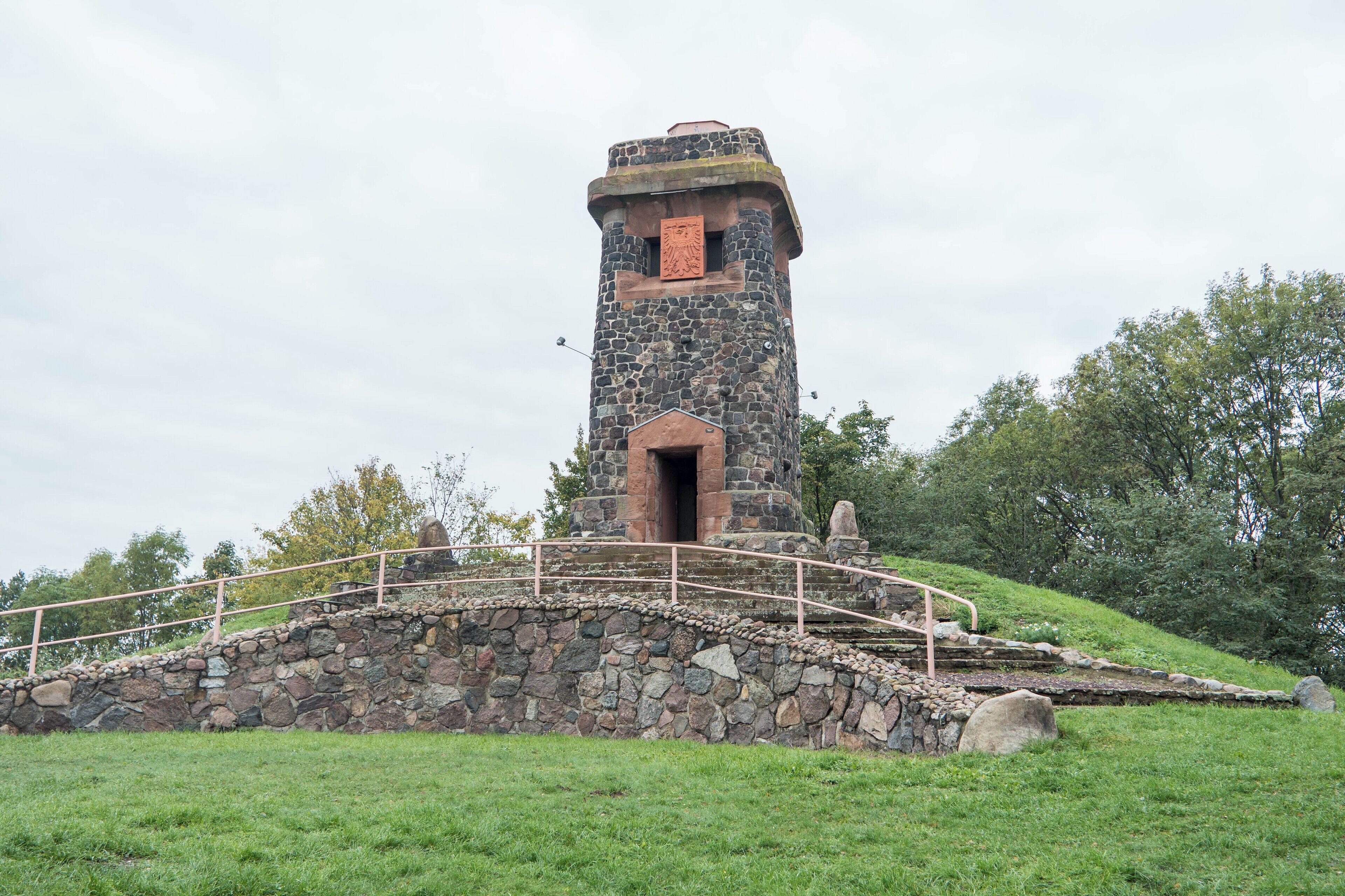 A stone tower with a metal bridge in a grassy area.