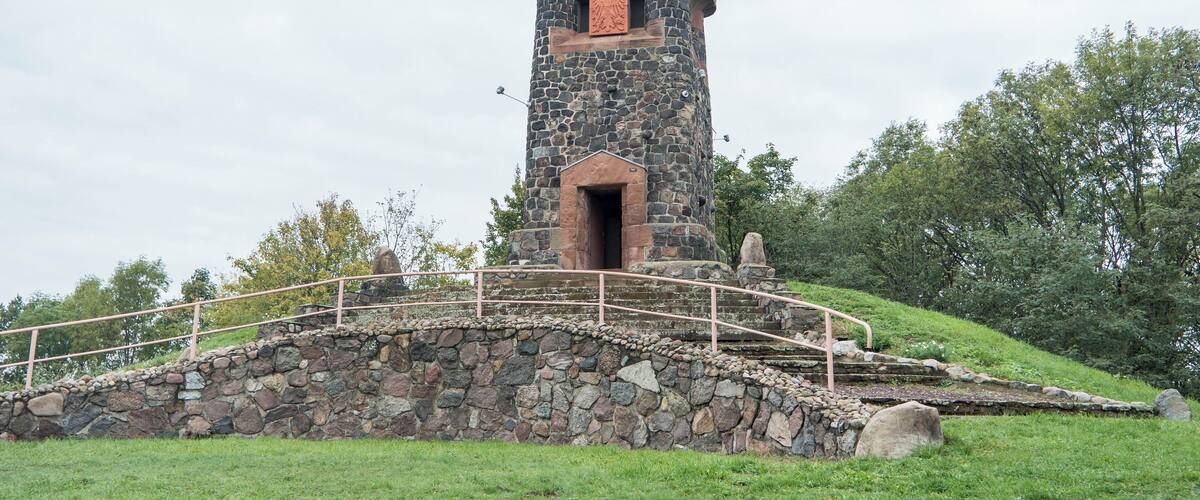 A stone tower with a metal bridge in a grassy area.