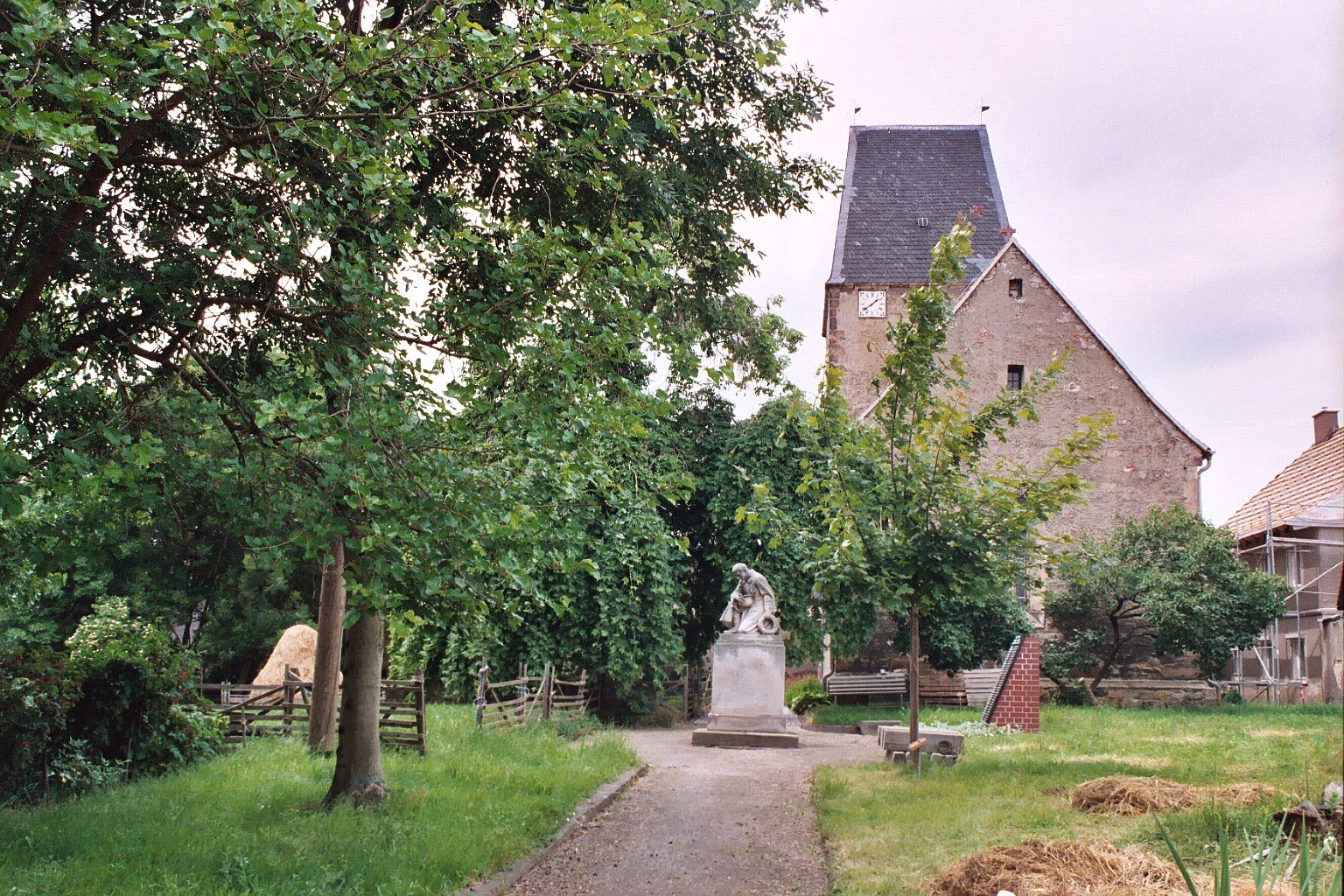 A rural landscape with a stone building, a statue, and a path leading to it.