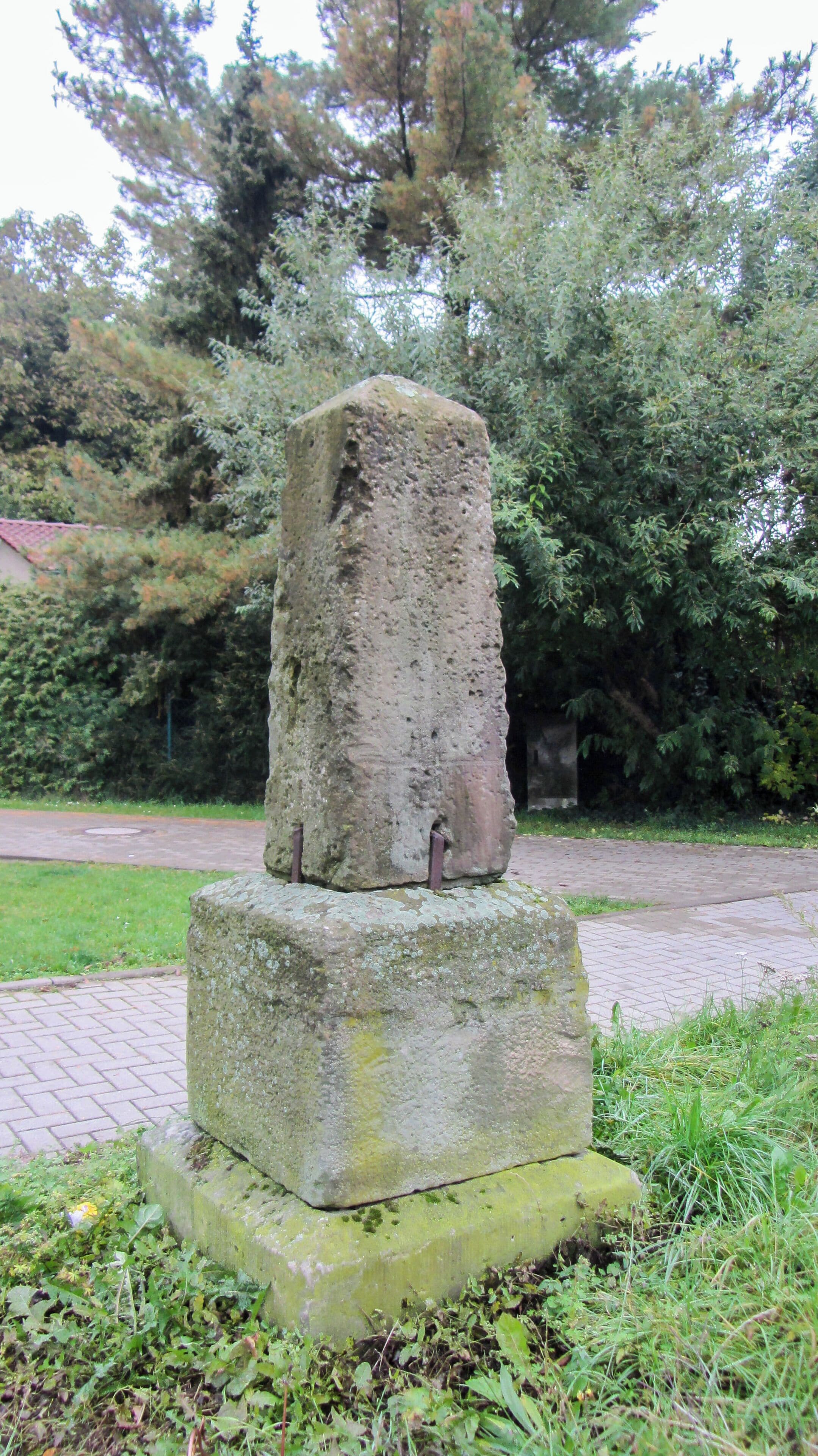 A weathered stone monument with moss growth, surrounded by lush greenery and trees.