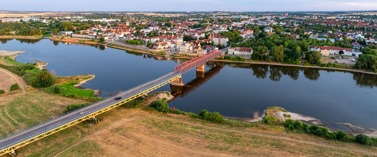 Ein Fluss mit einer Brücke, eine Stadt mit bunten Häusern und ein ferner Stadtblick.