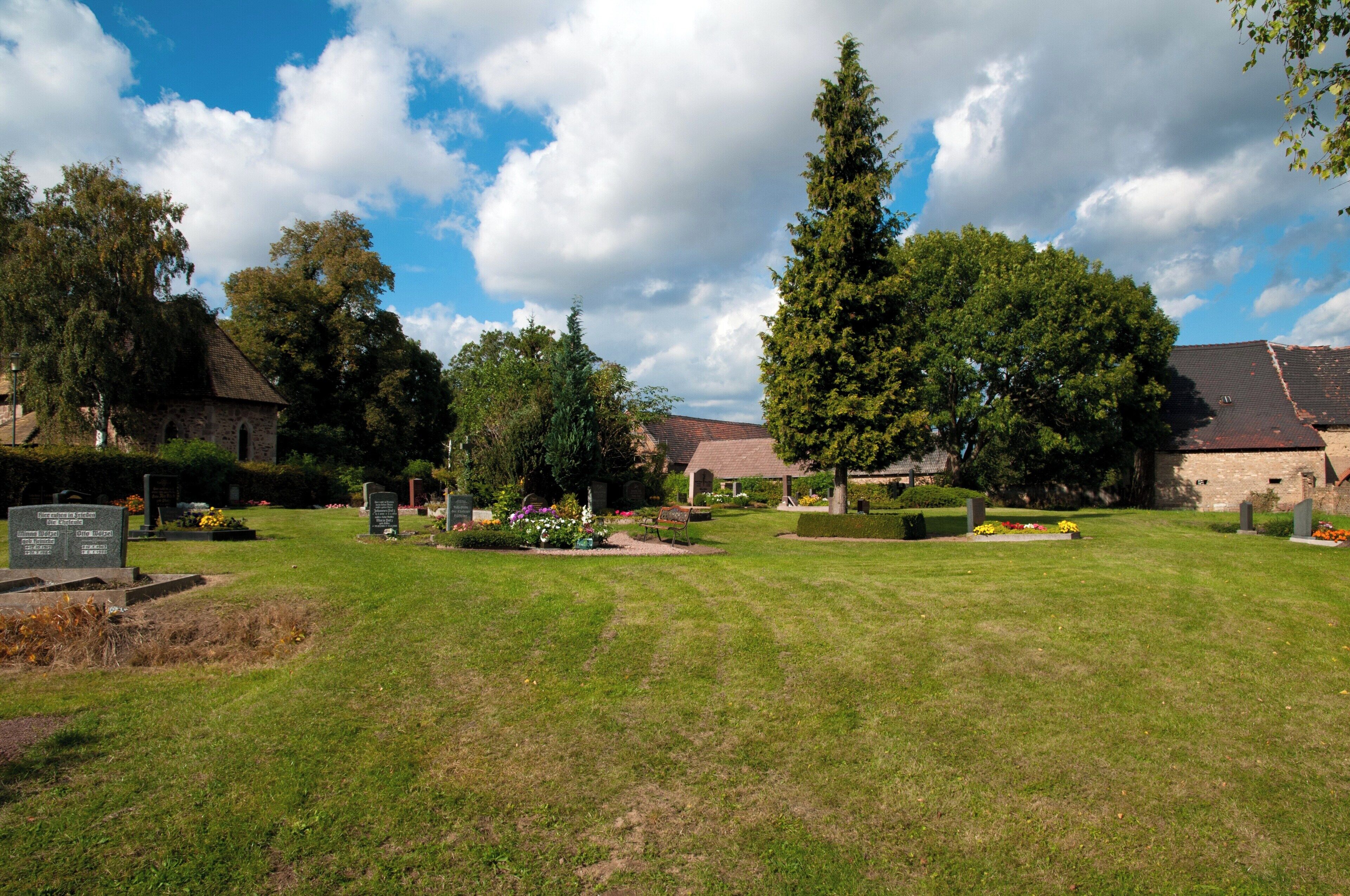 A cemetery with headstones, trees, and a clear sky.