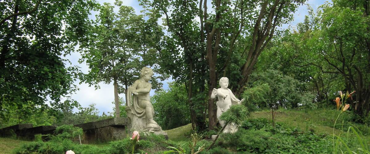 A garden with statues, pink roses, and lush greenery.