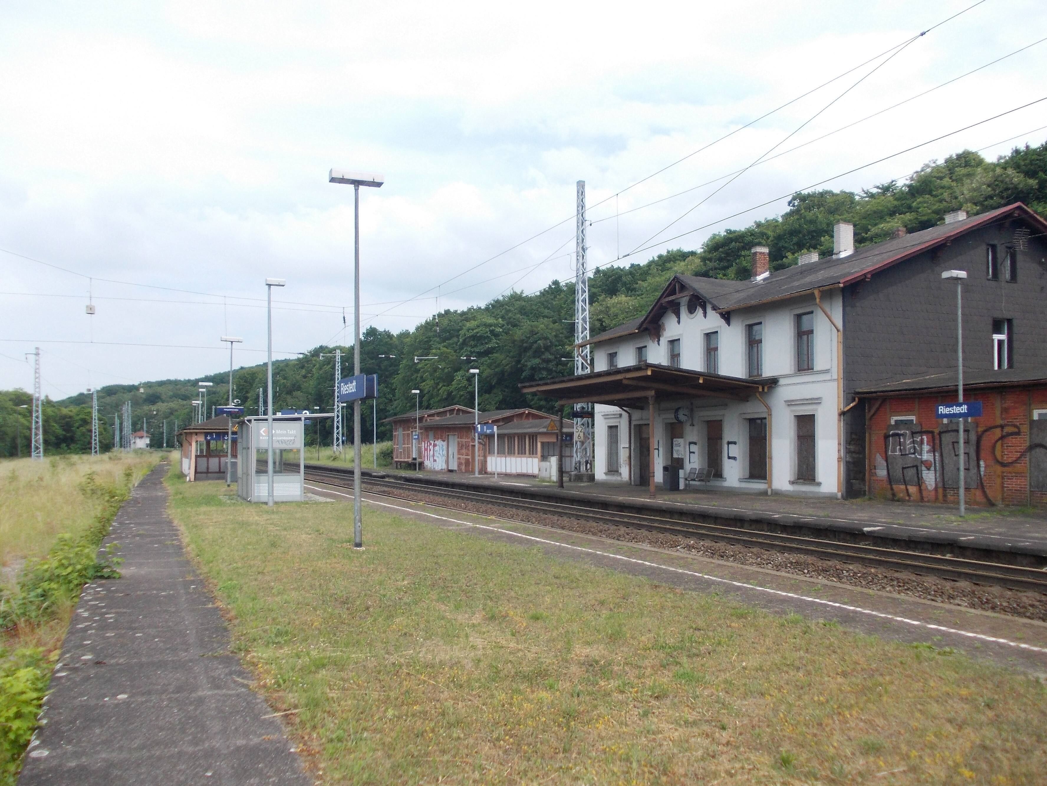 A train station with tracks, a platform, and buildings in the background.