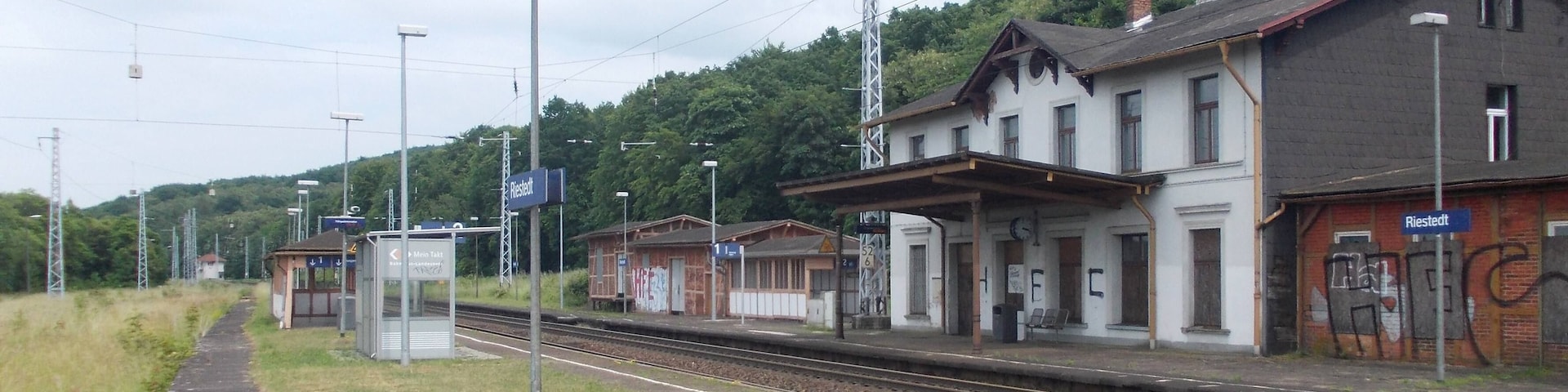 A train station with tracks, a platform, and buildings in the background.