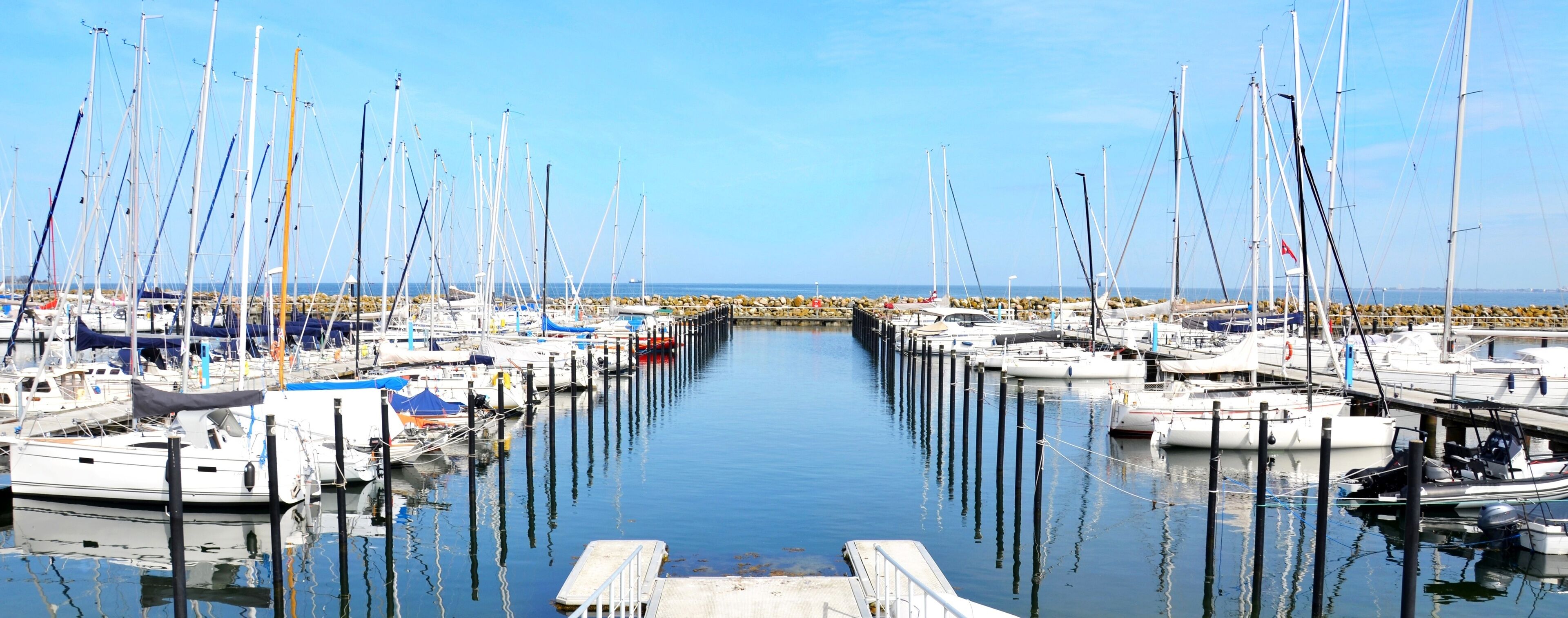 A marina with numerous sailboats docked along a calm waterway.