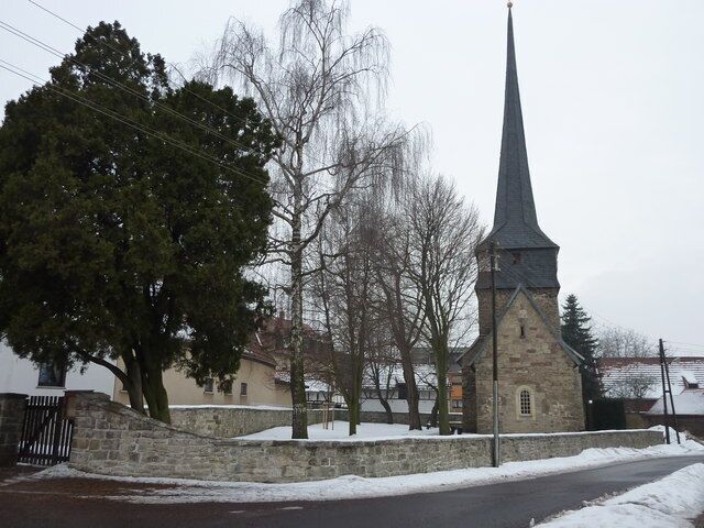 A church with a tall steeple, a stone wall, and bare trees.