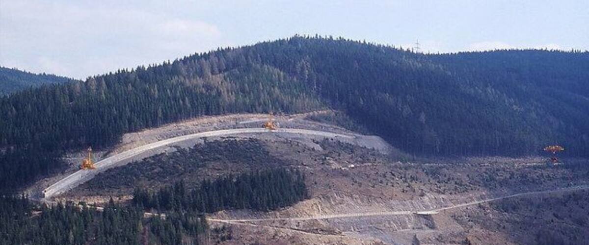 A mountainous landscape with a road cutting through it, surrounded by dense forests.