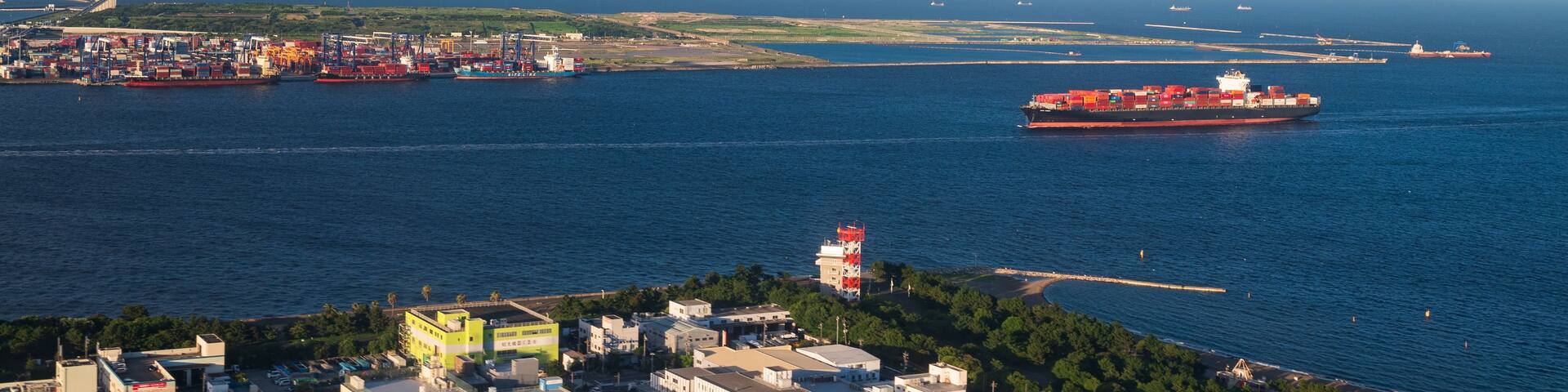 A coastal cityscape with a large cargo ship, a bridge, and a distant city skyline.