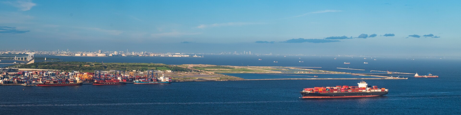 Un paisaje urbano costero con un gran carguero, un puente y una línea de horizonte de ciudad distante.
