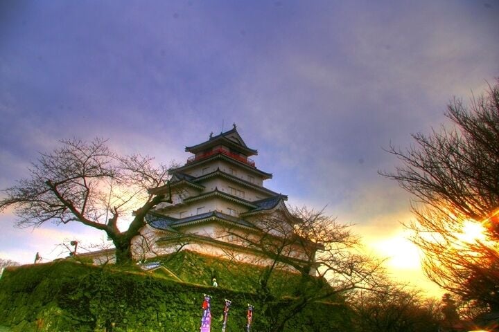 A traditional Japanese castle with multiple tiers, surrounded by lush greenery and trees.