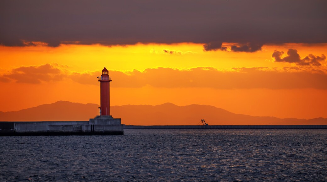Un faro al atardecer con una cadena montañosa al fondo.