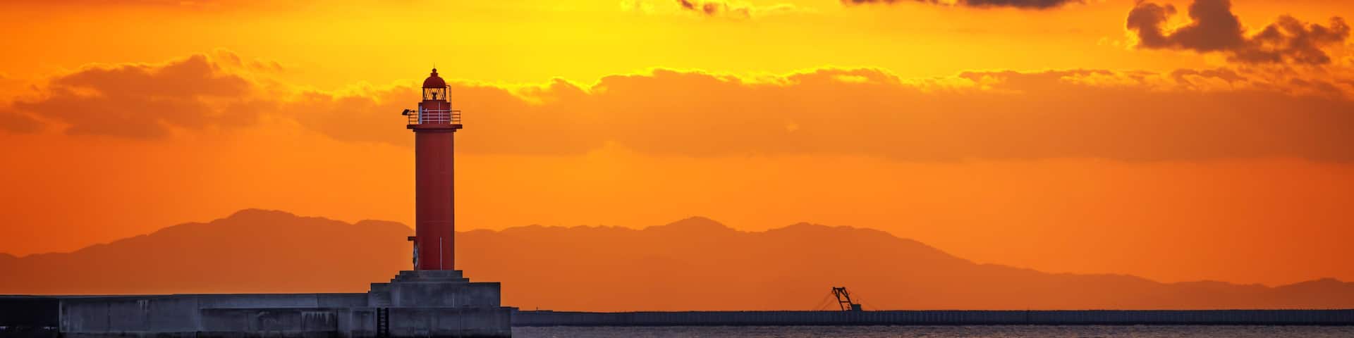 A lighthouse at sunset with a mountain range in the background.