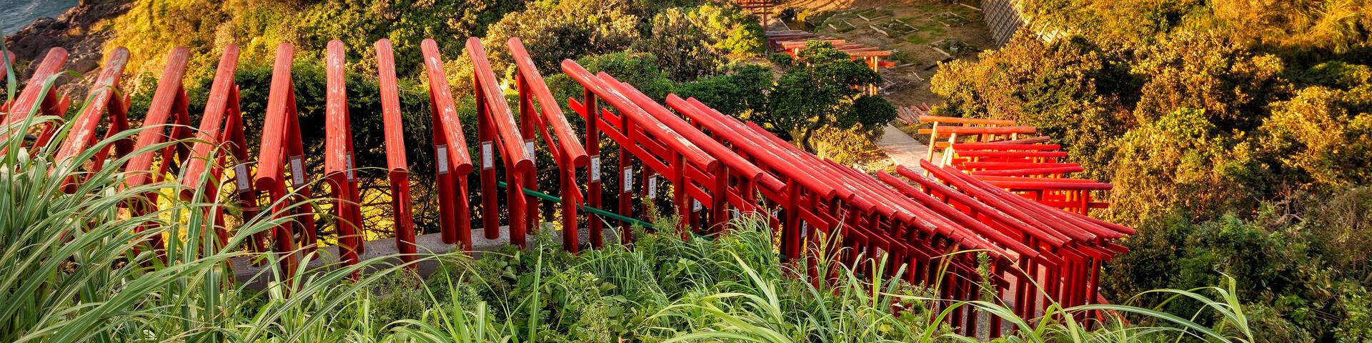 A coastal landscape with red torii gates, rocky cliffs, and a view of the sea.