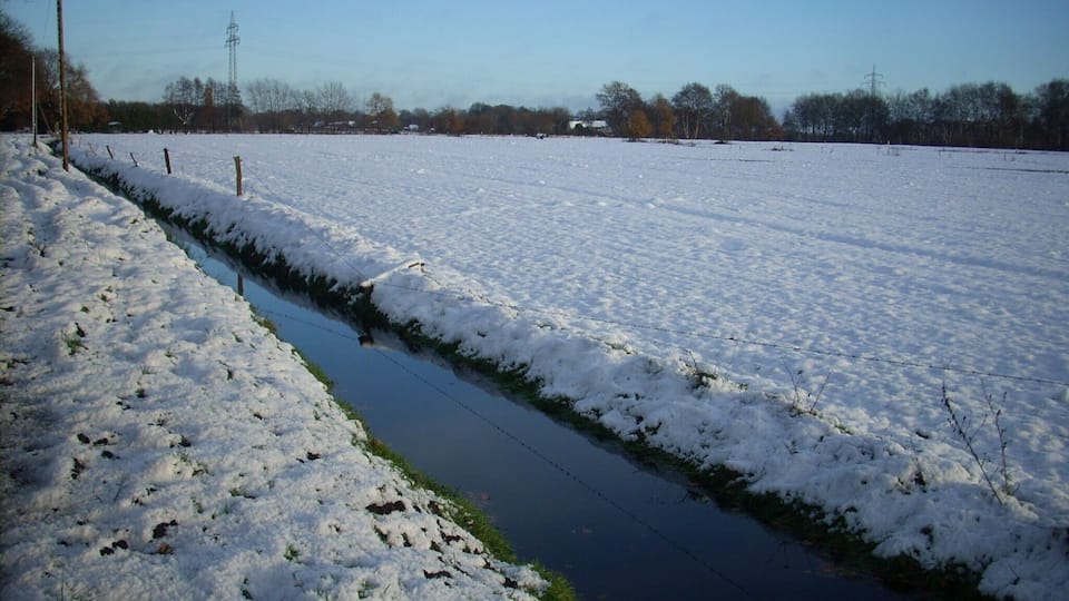 A snow-covered field with a narrow water channel running through it.