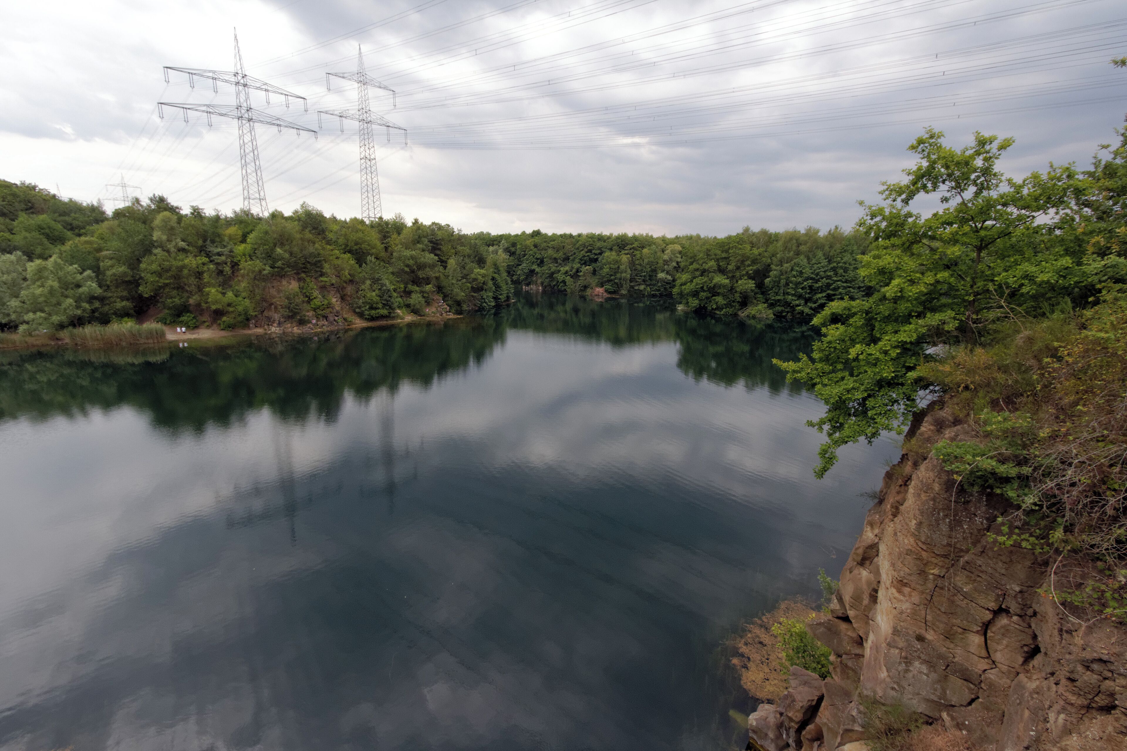 A calm lake surrounded by dense forest and power lines in the background.