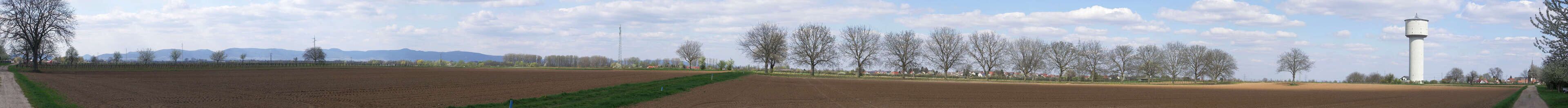 A rural landscape with fields, trees, a water tower, and distant mountains.