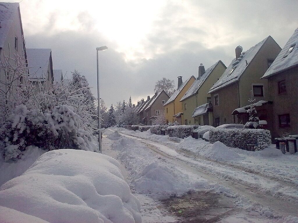 A snow-covered street with houses and a lamppost.