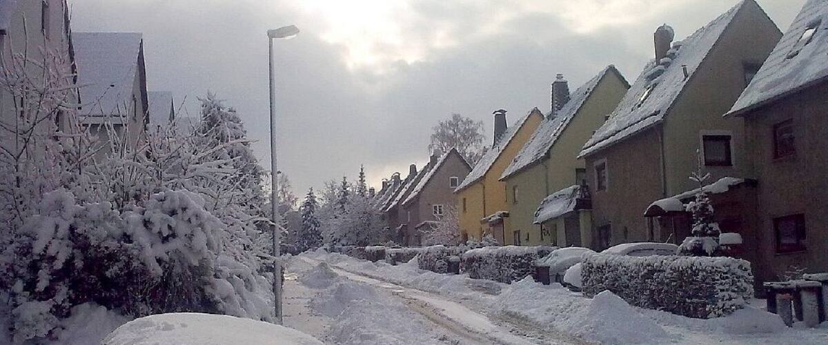 A snow-covered street with houses and a lamppost.