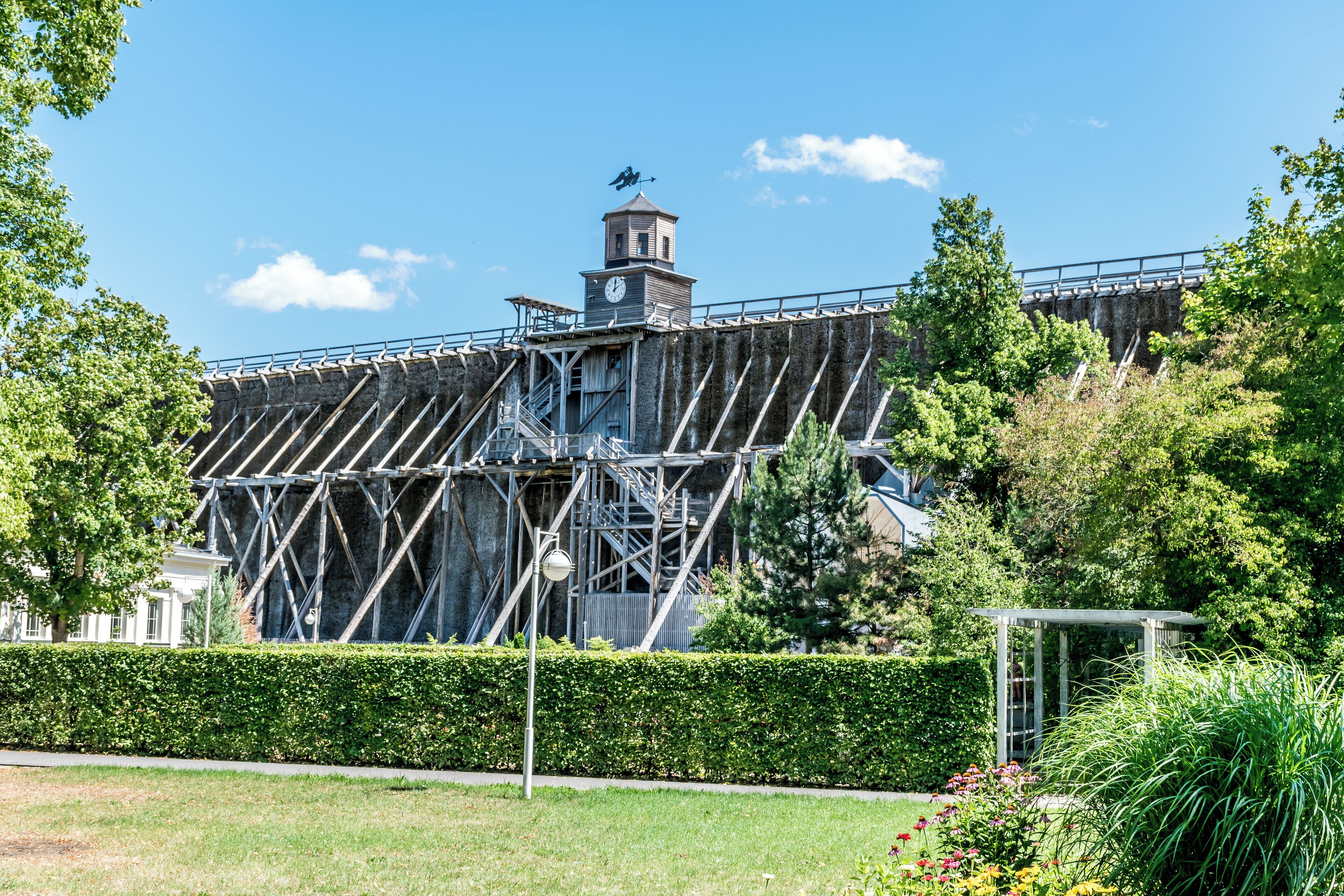 A large metal structure with a clock tower, surrounded by greenery and a garden.