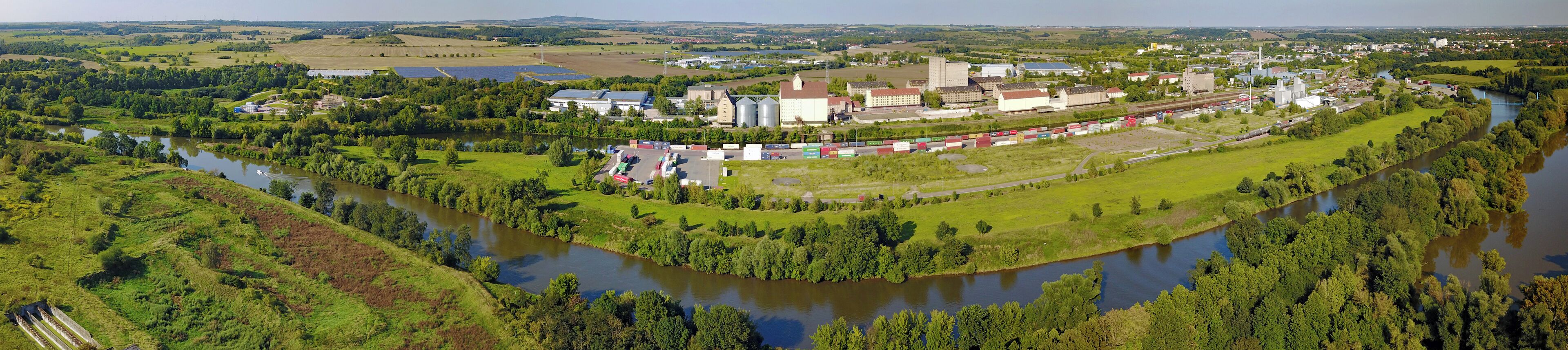 A river winding through a green landscape with industrial buildings and a train station.