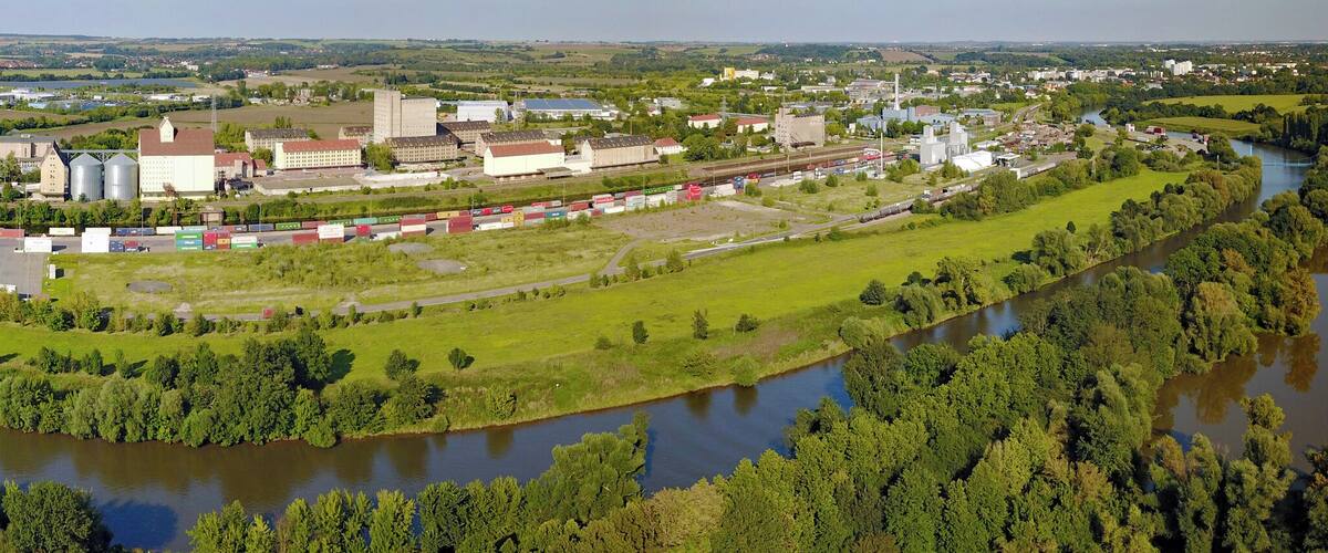 A river winding through a green landscape with industrial buildings and a train station.