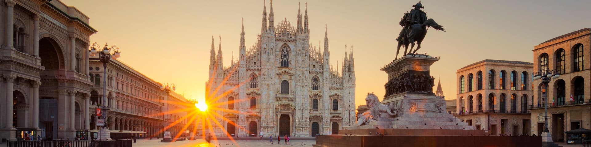 A cathedral with intricate Gothic architecture, a statue of a historical figure, and a clear sky with the sun setting.