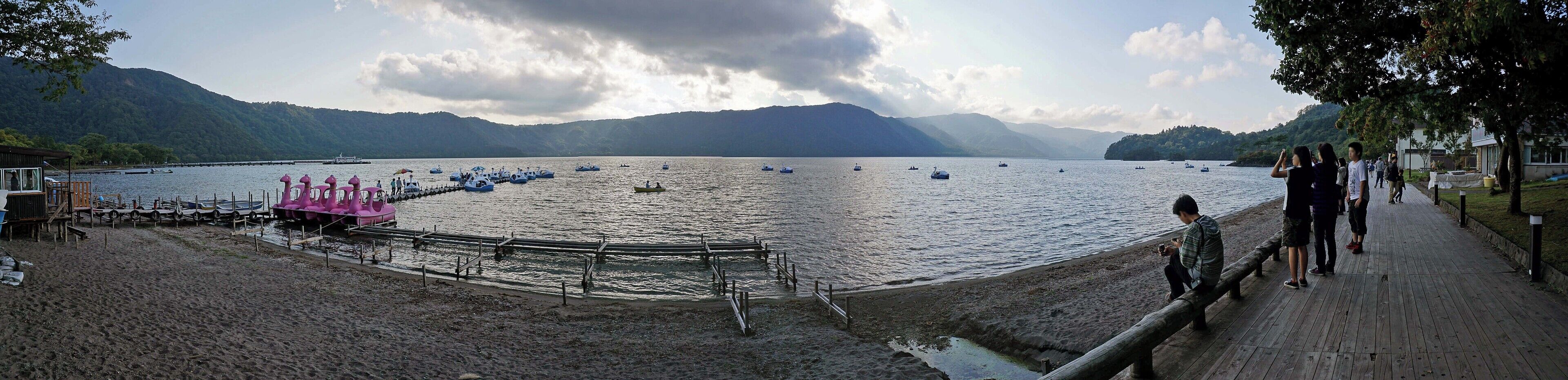 A lake with boats, a wooden dock, and mountains in the background.