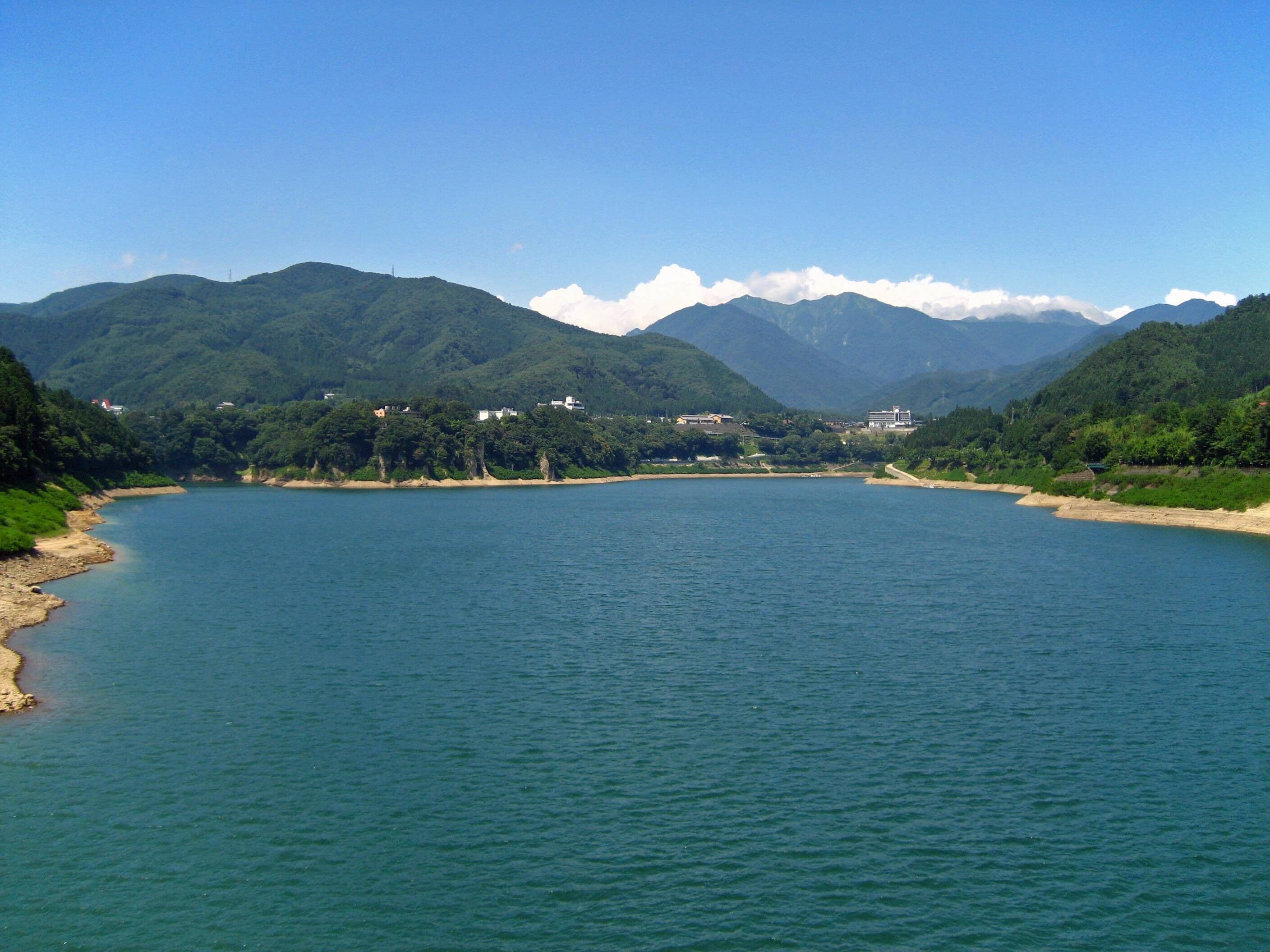 A calm river flanked by lush green hills and mountains under a clear blue sky.