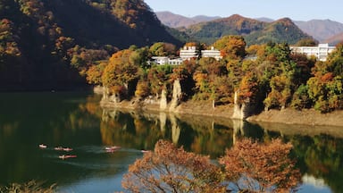 A calm lake with boats, surrounded by autumn-colored trees and a white building on a hillside.
