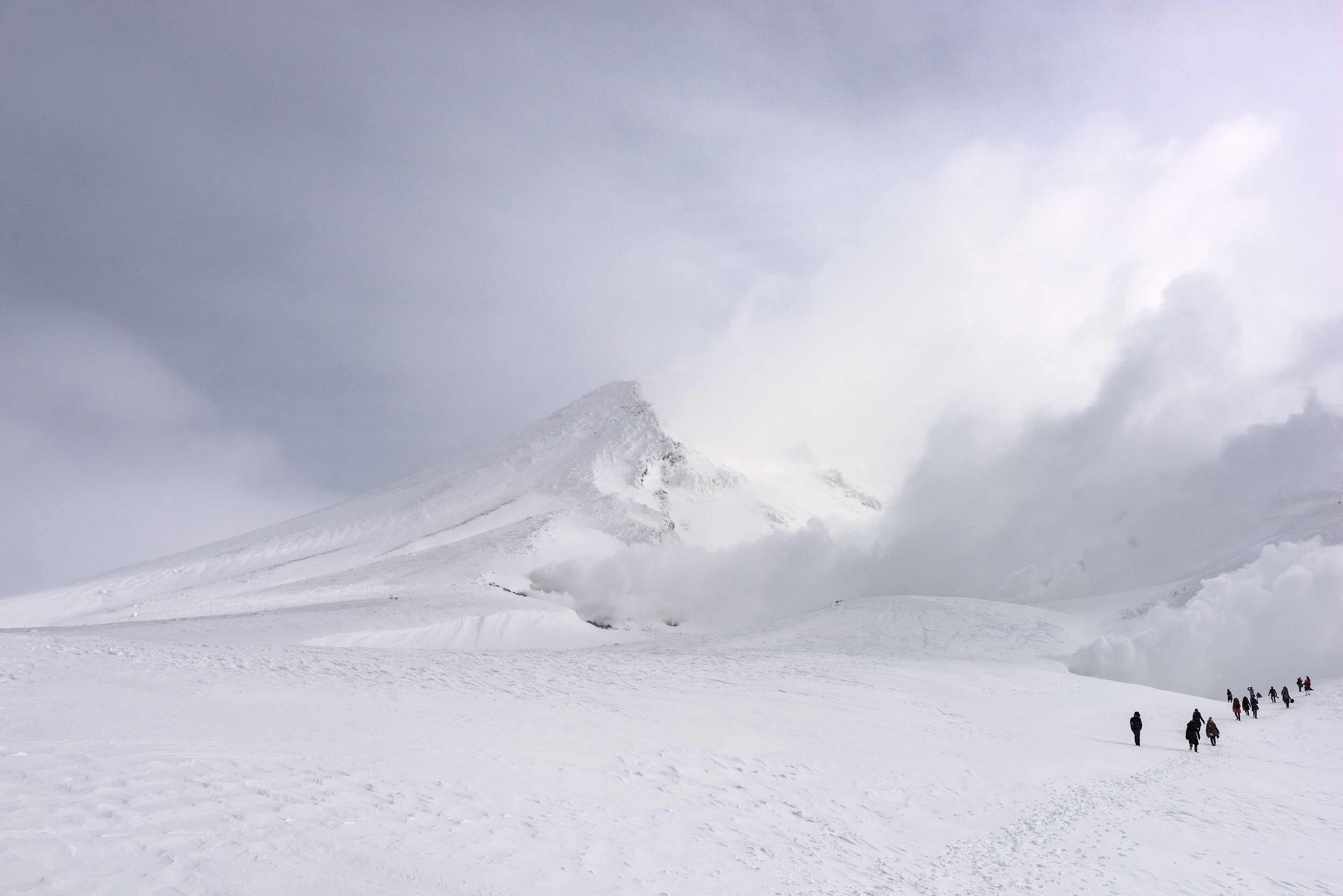 A snow-covered mountain with a group of people walking on a flat snowfield.