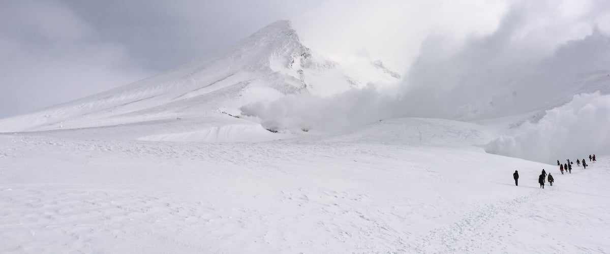 A snow-covered mountain with a group of people walking on a flat snowfield.