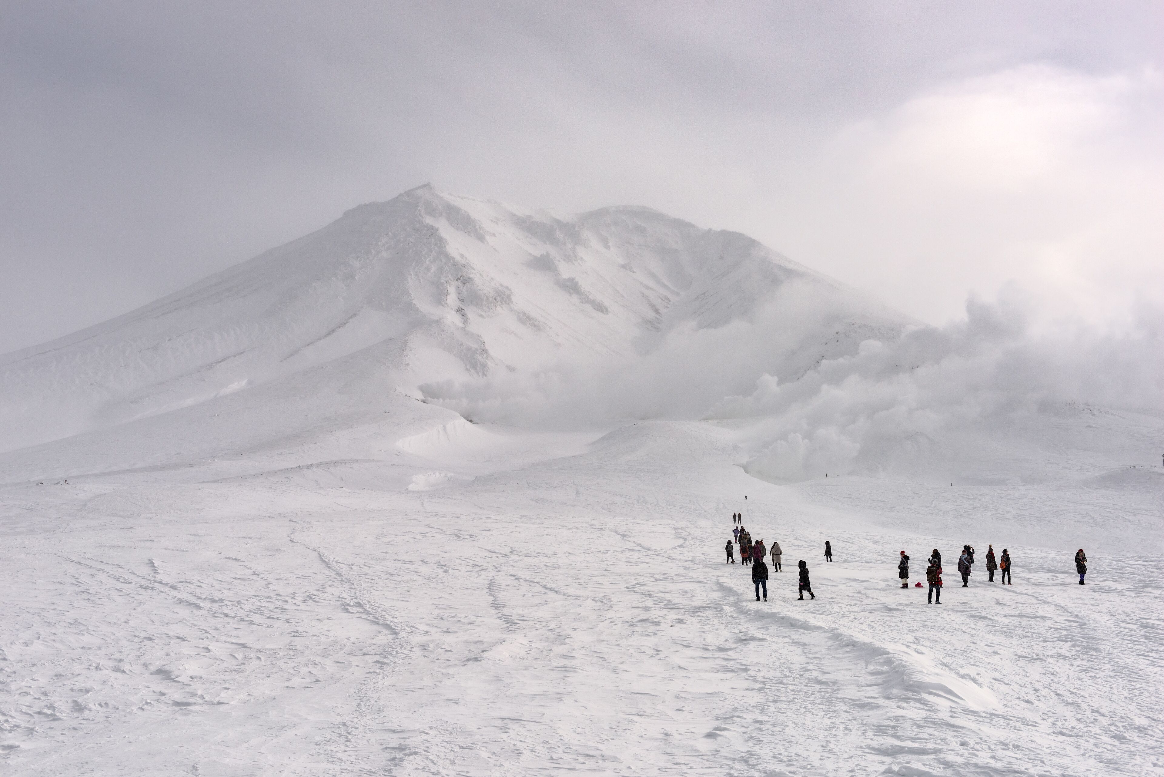 A snowy mountain landscape with a group of people walking on a snow-covered path.