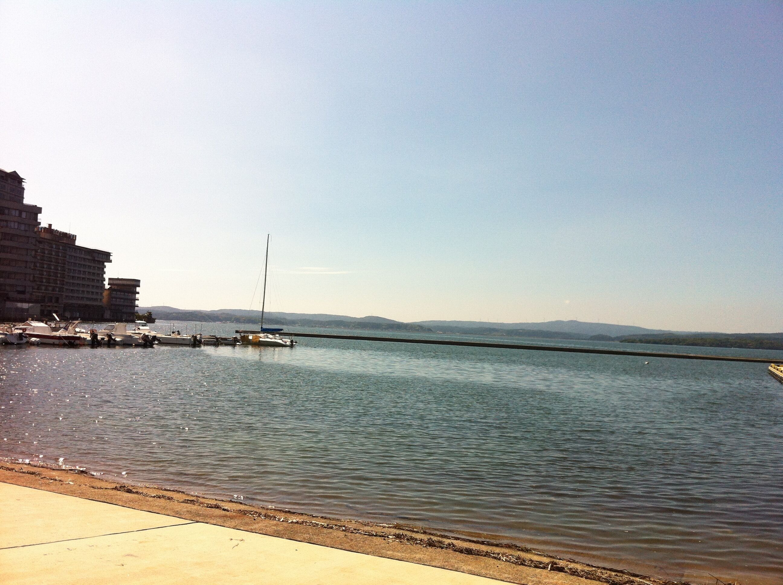 A waterfront with boats docked, a sailboat, and a building in the background.