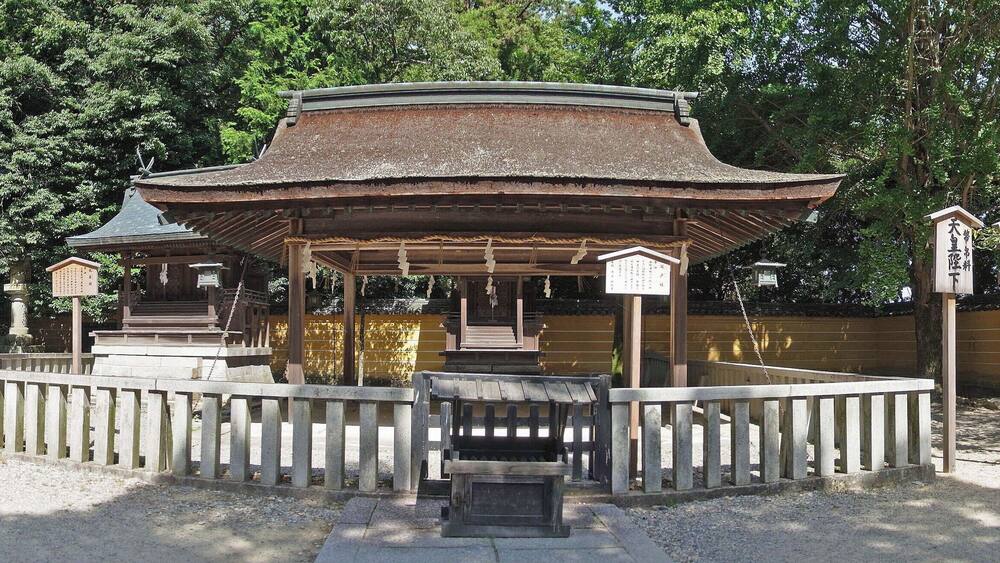 Un pavillon japonais traditionnel, entouré de lanternes en pierre et d’une clôture en bois.