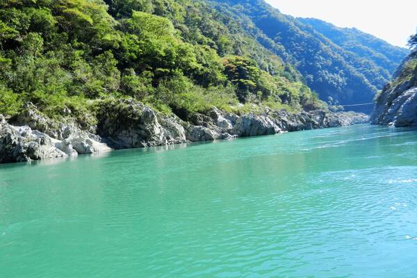 Um rio azul-turquesa serpenteando por uma paisagem montanhosa com margens rochosas e vegetação verde densa.