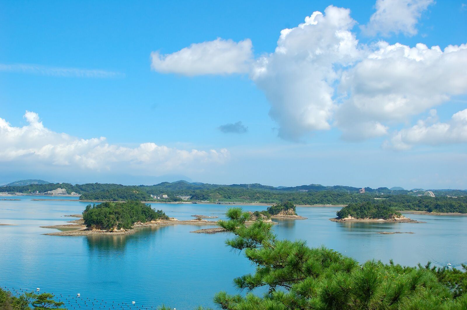 A calm river with several small islands, surrounded by lush greenery and distant hills.