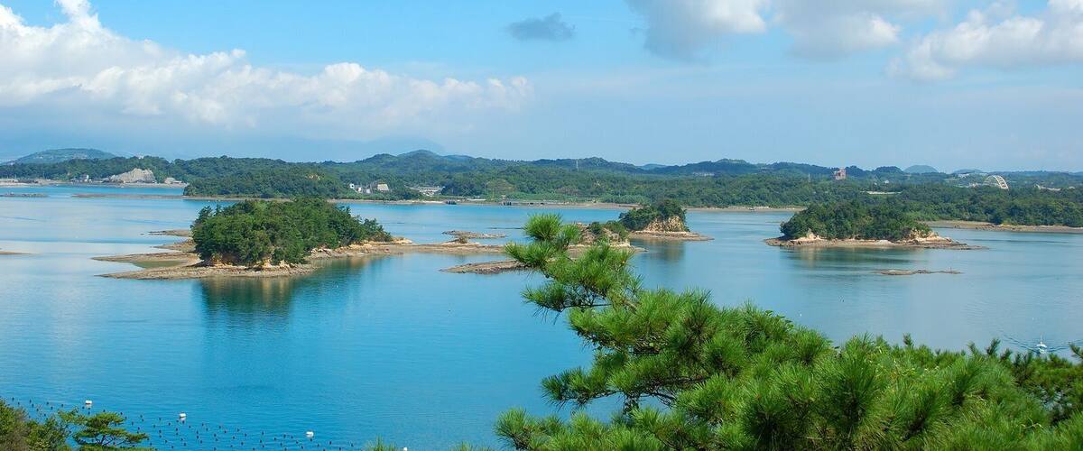 A calm river with several small islands, surrounded by lush greenery and distant hills.