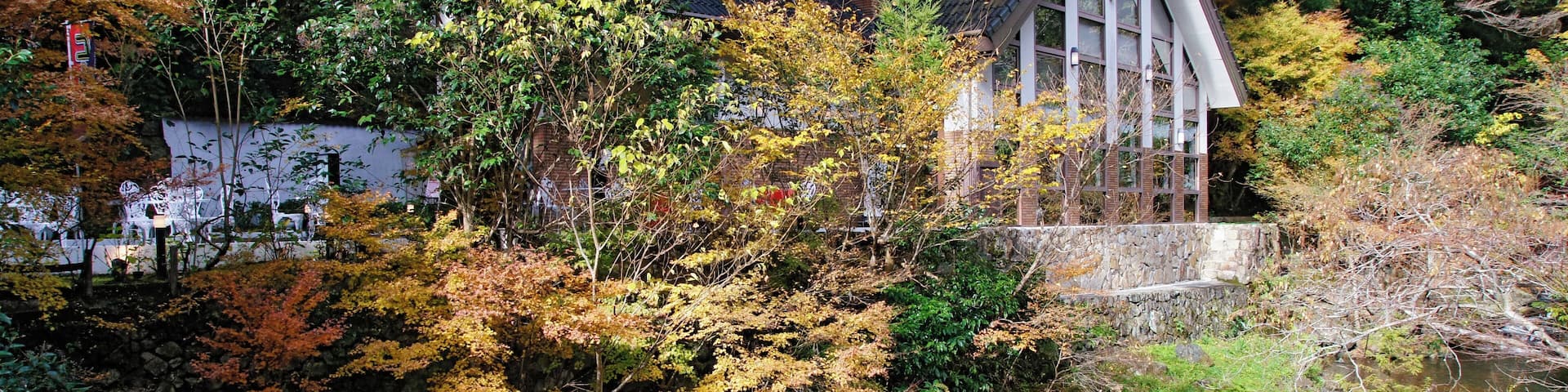 A traditional Japanese house nestled among autumn-colored trees and a flowing stream.
