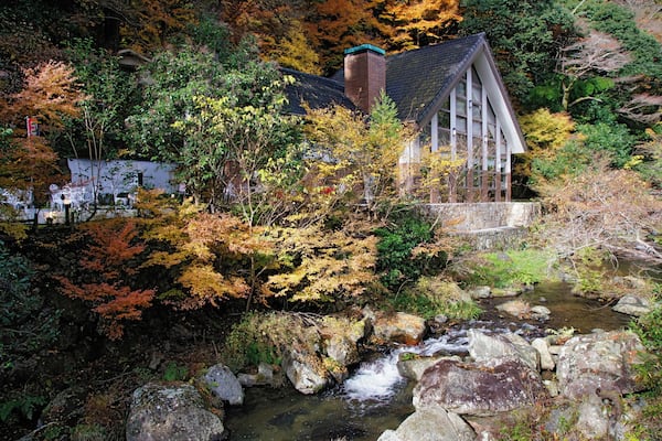 Ein traditionelles japanisches Haus, eingebettet zwischen herbstlich gefärbten Bäumen und einem plätschernden Bach.