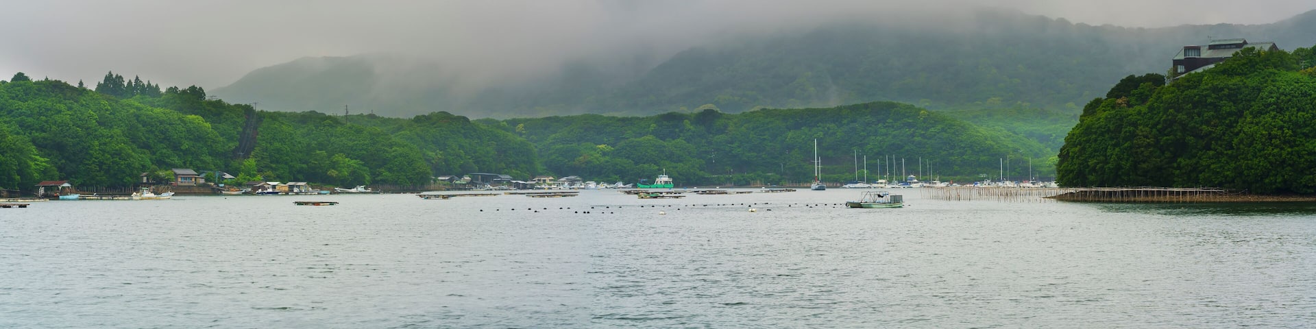 A coastal town with boats, a pier, and lush green hills in the background.