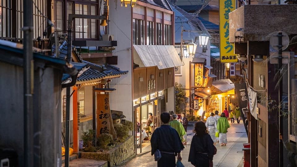 A narrow street with traditional buildings, a signboard with Japanese characters, and people walking.
