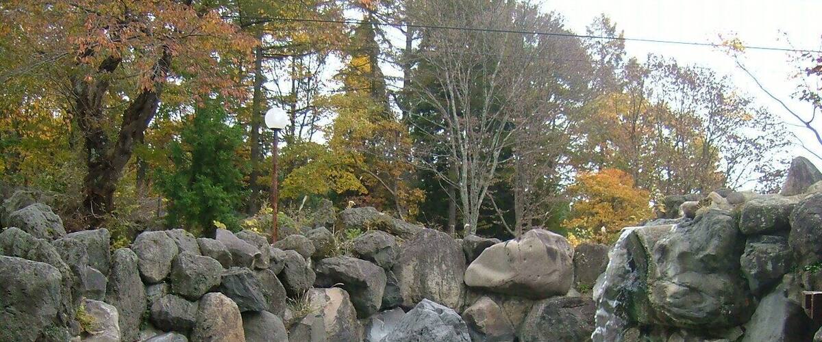 A clear pond surrounded by large rocks and autumn-colored trees.