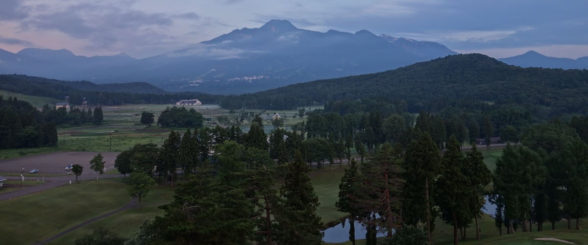 A mountainous landscape with a golf course in the foreground and a large building in the middle distance.