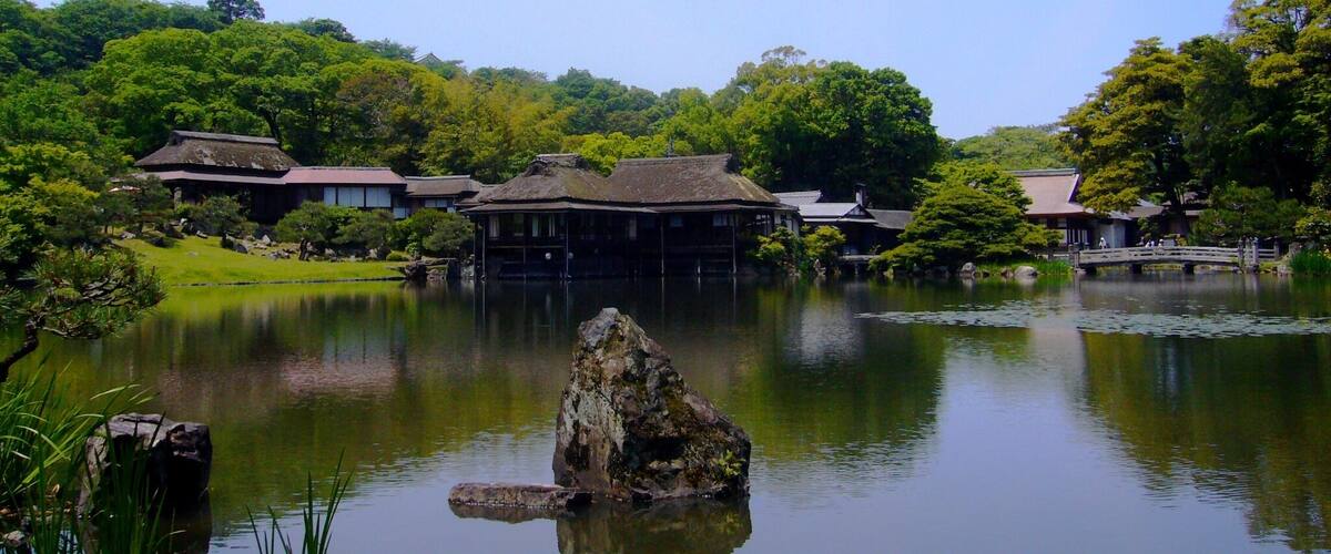 A traditional Japanese building by a calm pond with a rock in the center.