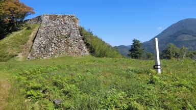 A stone pyramid structure surrounded by lush greenery and a clear blue sky.