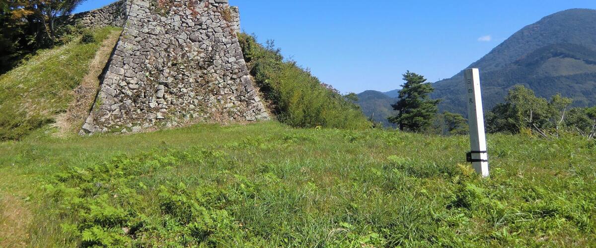 A stone pyramid structure surrounded by lush greenery and a clear blue sky.