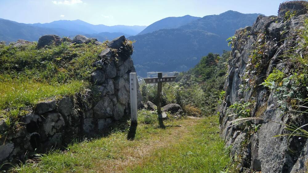 Ein Steinweg führt durch eine gebirgige Landschaft, ein Wegweiser zeigt die Richtungen.